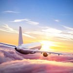 Airplane flying above clouds during sunset sky