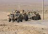 Soldiers standing near armored vehicles in desert terrain.