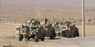 Soldiers standing near armored vehicles in desert terrain.