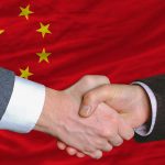 Two people shaking hands, Chinese flag background.