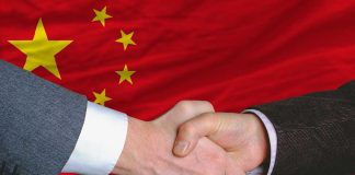 Two people shaking hands, Chinese flag background.