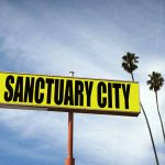 "Sanctuary City" sign with palm trees and sky.