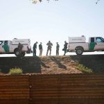 Border patrol agents near vehicles on embankment daytime