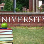 Books and apple in front of university sign