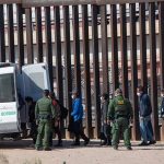 Border patrol agents detaining individuals near a fence