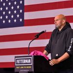 Person speaking at podium with American flag backdrop