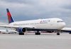 Delta Airlines airplane on airport runway, cloudy sky.