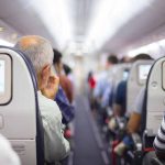 Passengers seated in airplane cabin with screens visible