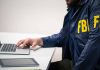 Person in FBI jacket using laptop at desk