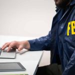 Person in FBI jacket using laptop at desk