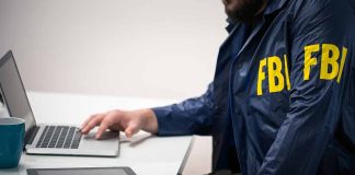 Person in FBI jacket using laptop at desk