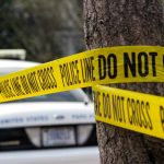 Yellow police tape around tree near car