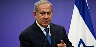 Prime minister Benjamin Netanyahu pointing to the camera in front of Israeli flag