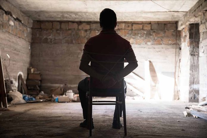 Person tied to chair in dimly lit room.