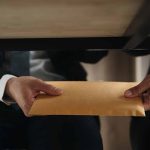 Two people exchanging envelope under table.