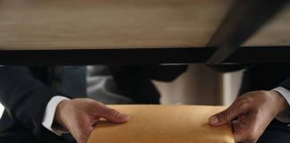 Two people exchanging envelope under table.