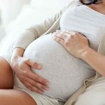 Pregnant woman holding her belly, sitting comfortably.