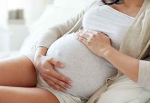 Pregnant woman holding her belly, sitting comfortably.