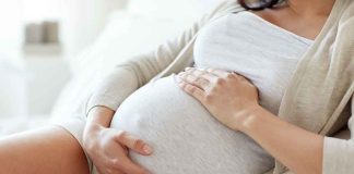 Pregnant woman holding her belly, sitting comfortably.