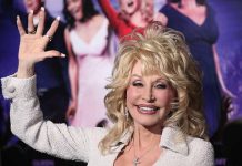 Dolly Parton smiling and waving in front of a crowd of people