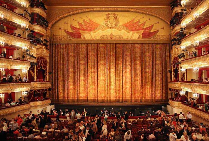 Ornate theater, grand curtain, audience seated below balconies.