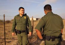 Two uniformed officers standing outdoors near a fence.