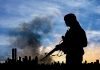 Silhouette of armed person with cityscape background smoke