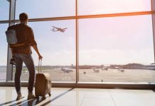 Traveler with luggage watches airplane take off at airport.