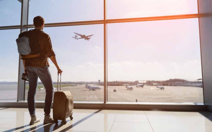 Traveler with luggage watches airplane take off at airport.