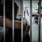 Person sitting behind jail bars with head down