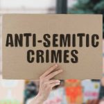 hand holding up a sign reading anti-semitic crimes
