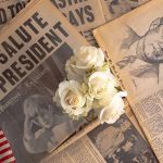 white flower on top of old newspapers featuring images of John F Kennedy