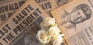 white flower on top of old newspapers featuring images of John F Kennedy