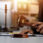 Hand holding gavel with scales in background.