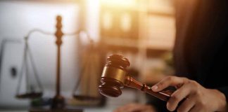 Hand holding gavel with scales in background.