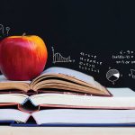 Apple on books with math equations on blackboard