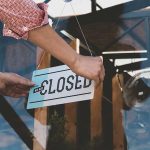 Hand placing closed sign on glass door