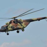 Camouflage military helicopter in flight against blue sky