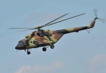 Camouflage military helicopter in flight against blue sky
