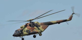 Camouflage military helicopter in flight against blue sky
