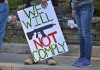 Protest sign reads We Will Not Comply