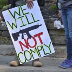 Protest sign reads We Will Not Comply