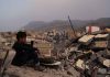 Boy amidst rubble with cityscape and mountains in background
