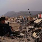 Boy amidst rubble with cityscape and mountains in background