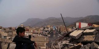 Boy amidst rubble with cityscape and mountains in background