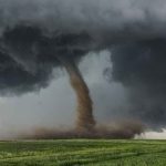 Tornado touching down in a grassy field.