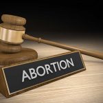 Gavel and sign reading Abortion on a wooden surface