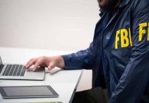 Person in FBI jacket using laptop at desk