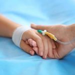 Two hands holding one with medical IV attached