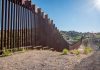 Tall metal border wall with rural landscape